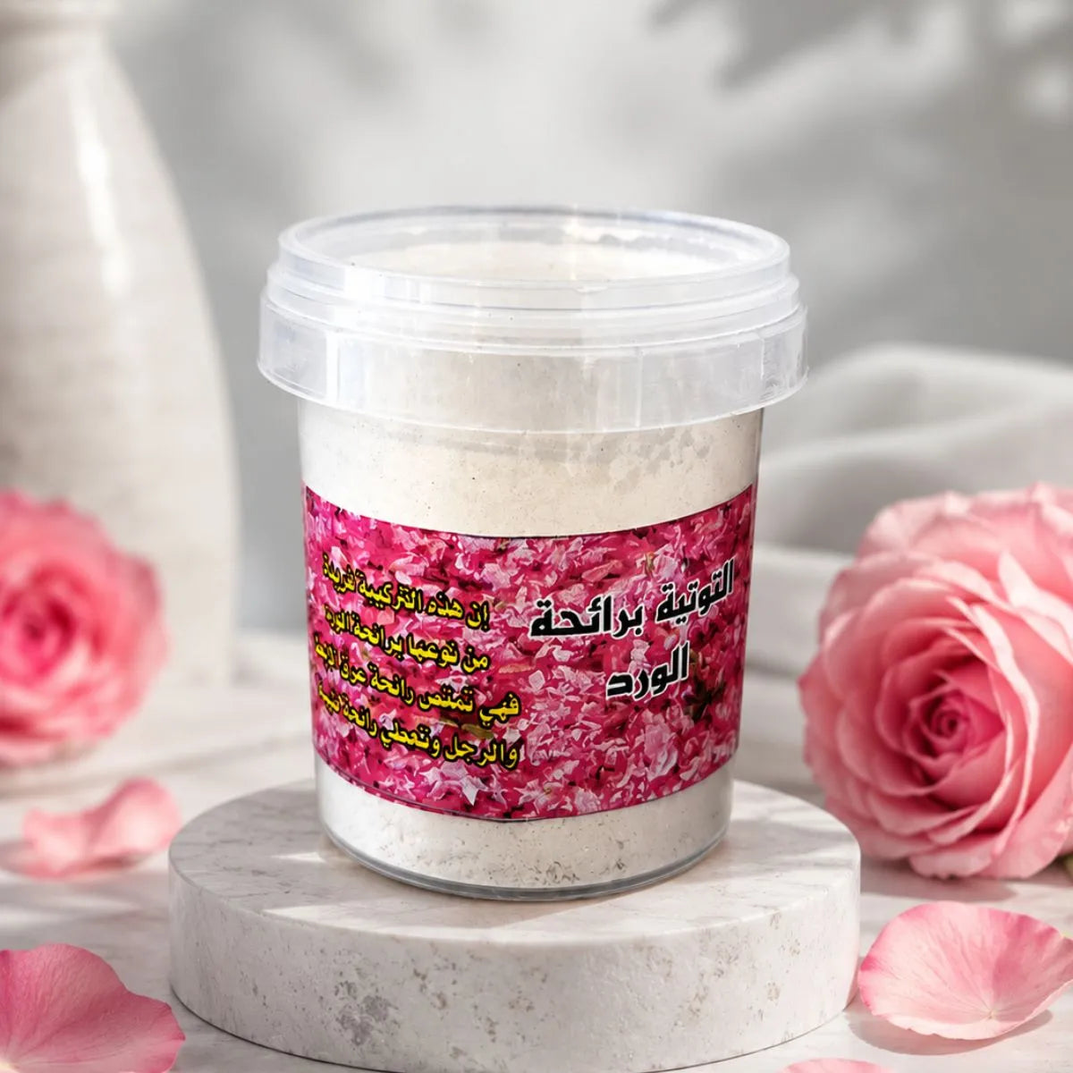 Poudre parfumée à la rose dans un pot transparent, nettoyant naturel multifonction pour la maison, présentée sur un support en marbre avec pétales et roses roses en arrière-plan.